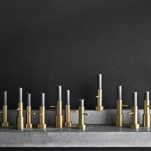 Cargar imagen en el visor de la galería, Row of gold and silver candle holders on a dark background