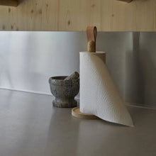 Cargar imagen en el visor de la galería, Roll of paper towels on a wooden holder next to a mortar and pestle on a kitchen counter.