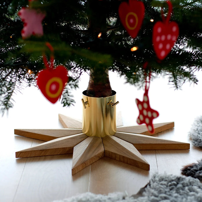 Wooden star-shaped tree stand with wood and brass base under a Christmas tree with red heart and star decorations.