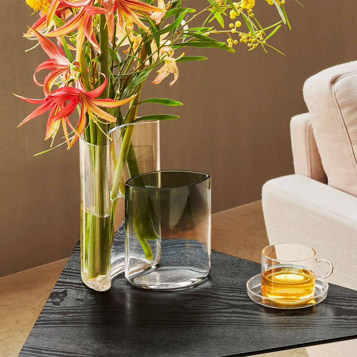 Clear glass vases with colorful flowers on a dark wooden table, with a beige sofa in the background.