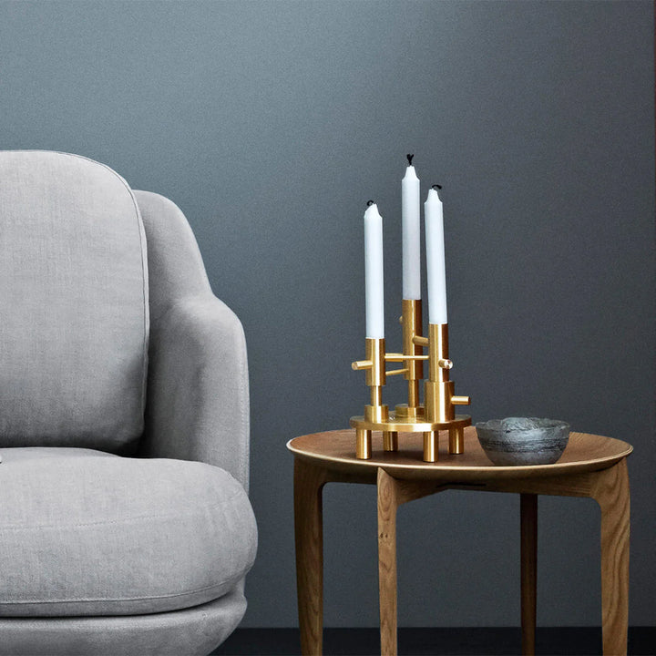 Gold candle holder with white candles on a wooden side table next to a gray armchair against a dark blue wall.