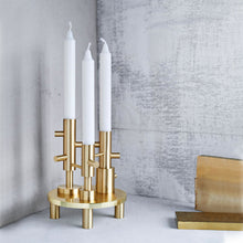 Cargar imagen en el visor de la galería, Gold candle holder with white candles against a gray concrete wall.
