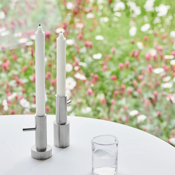 Two white candles in metal holders on a table with a blurred floral background