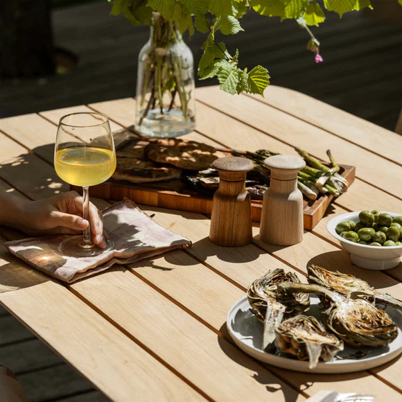 Person holding a glass of white wine at a wooden table with oysters, green olives, and a bottle of wine.