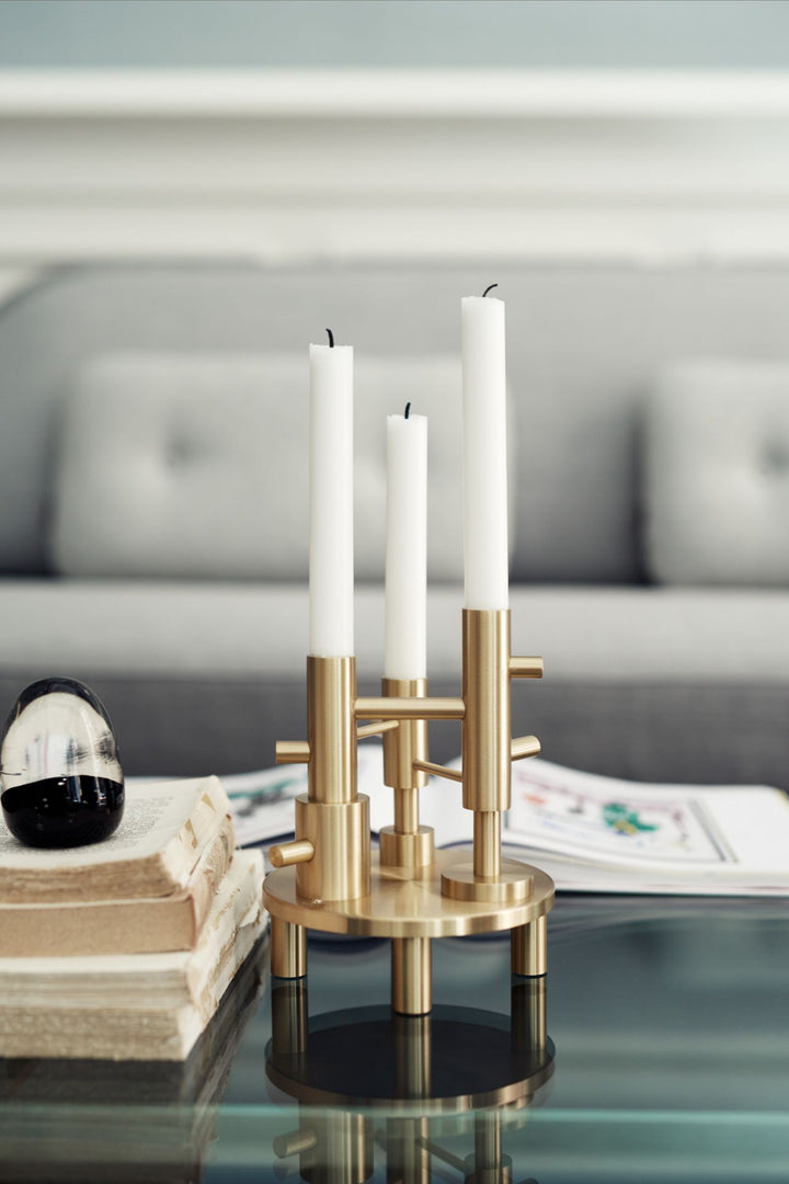 Gold candle holder with white candles on a glass table