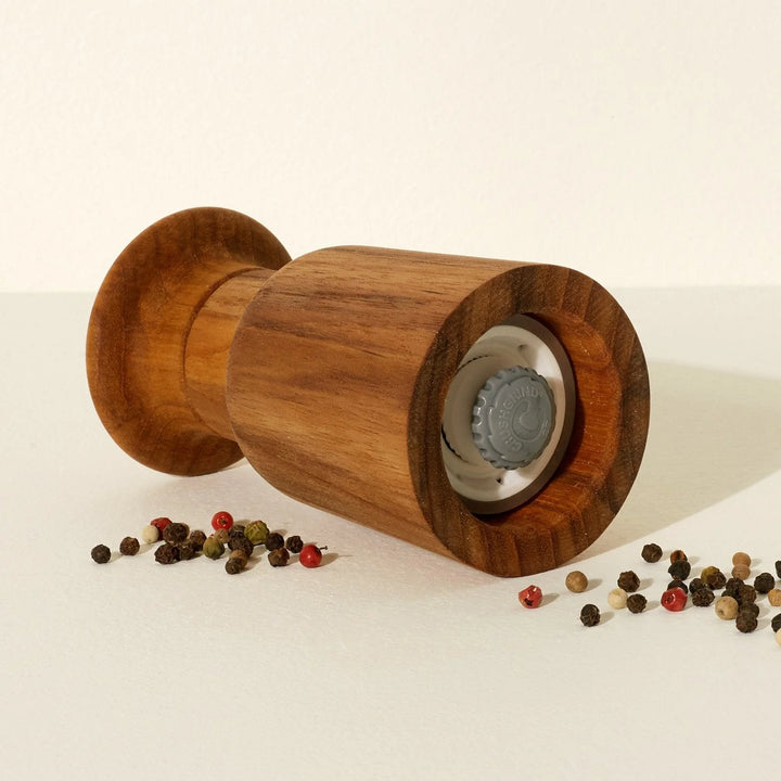 Wooden pepper grinder with peppercorns on a light background