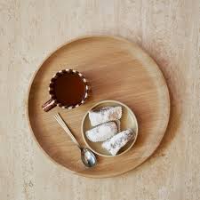 Wooden plate with a small bowl of cookies, a spoon, and a chocolate bar on a beige background