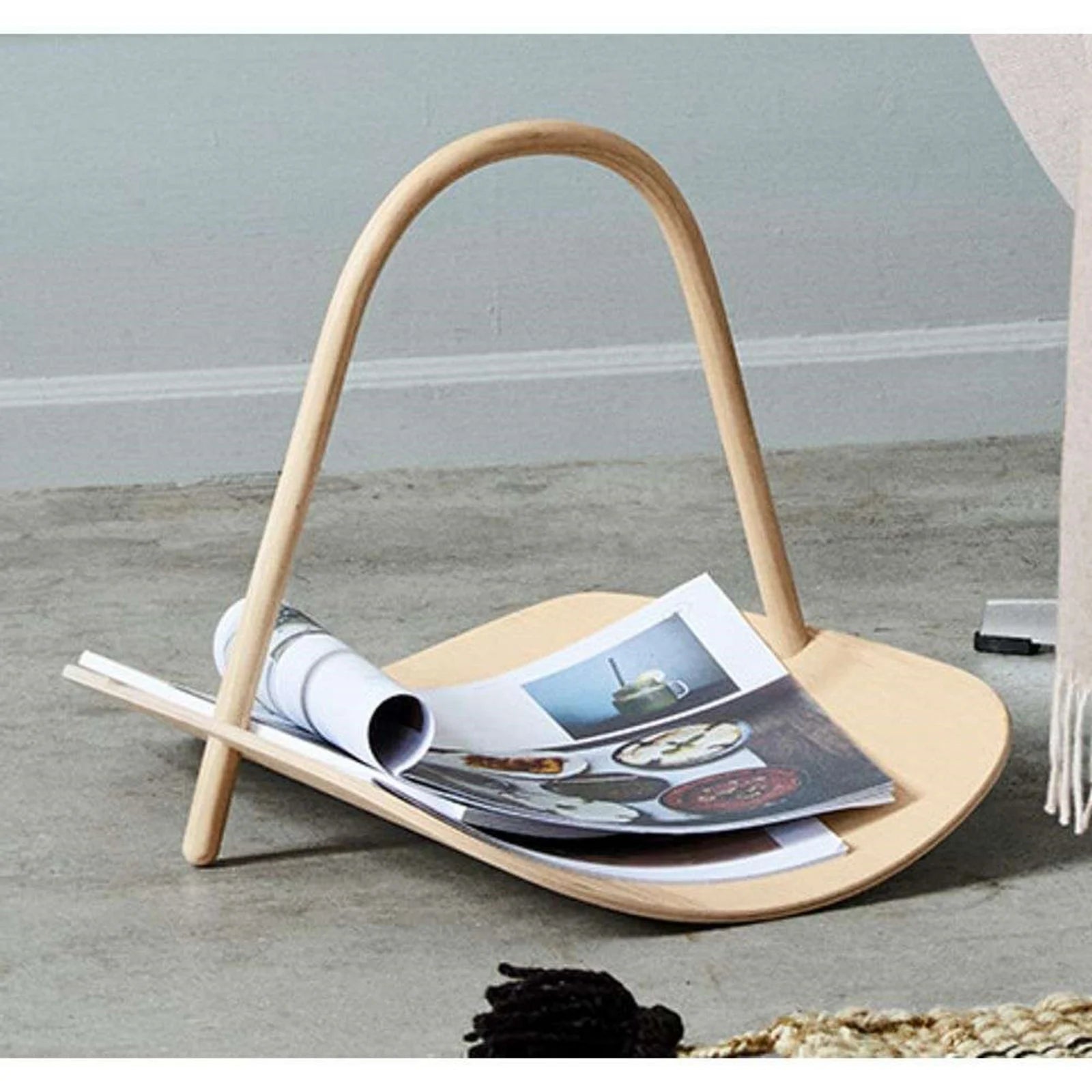 Wooden magazine holder with magazines on a gray floor.
