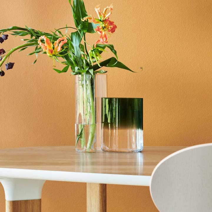 Clear glass vase with flowers on a wooden table against an orange wall