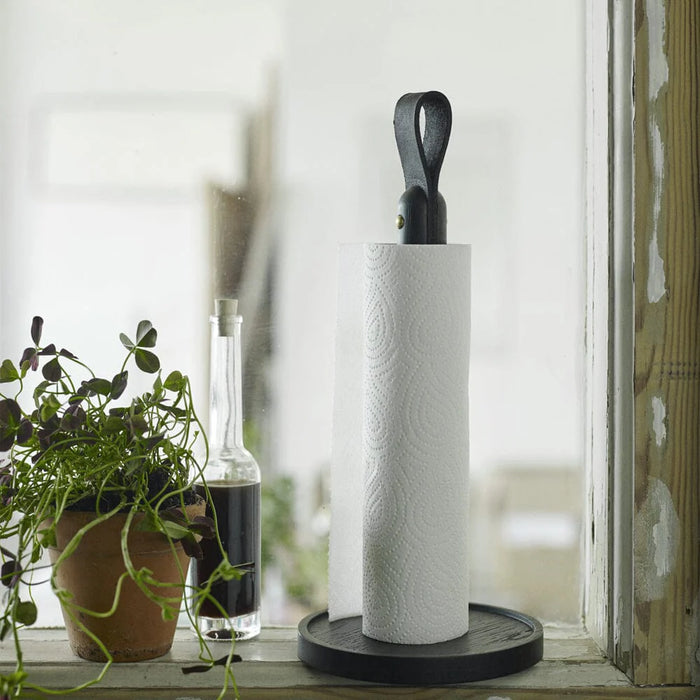 Roll of paper towels on a stand with a plant and bottle in the background