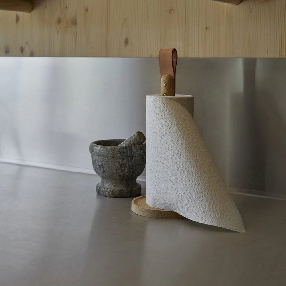 Roll of paper towels on a wooden holder next to a mortar and pestle on a kitchen counter.