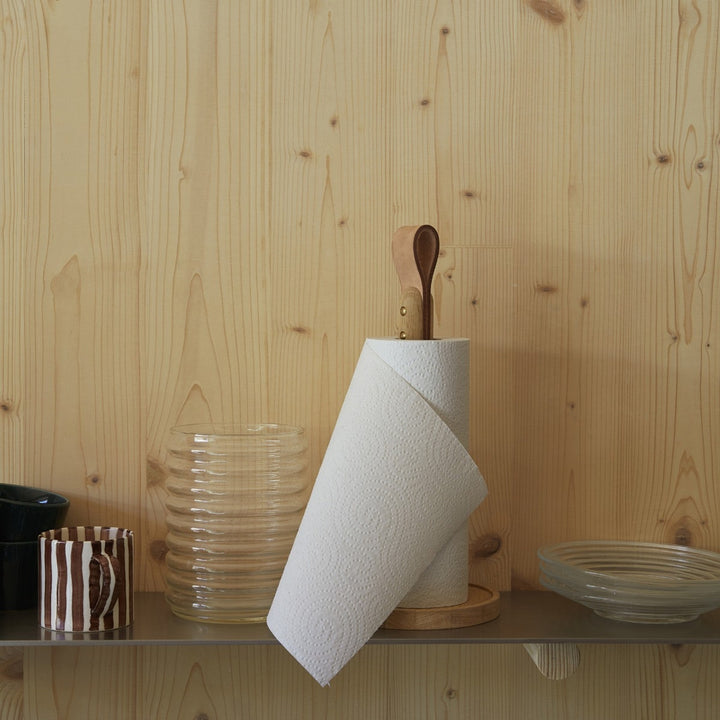 Roll of paper towels on a wooden stand against a wooden wall.