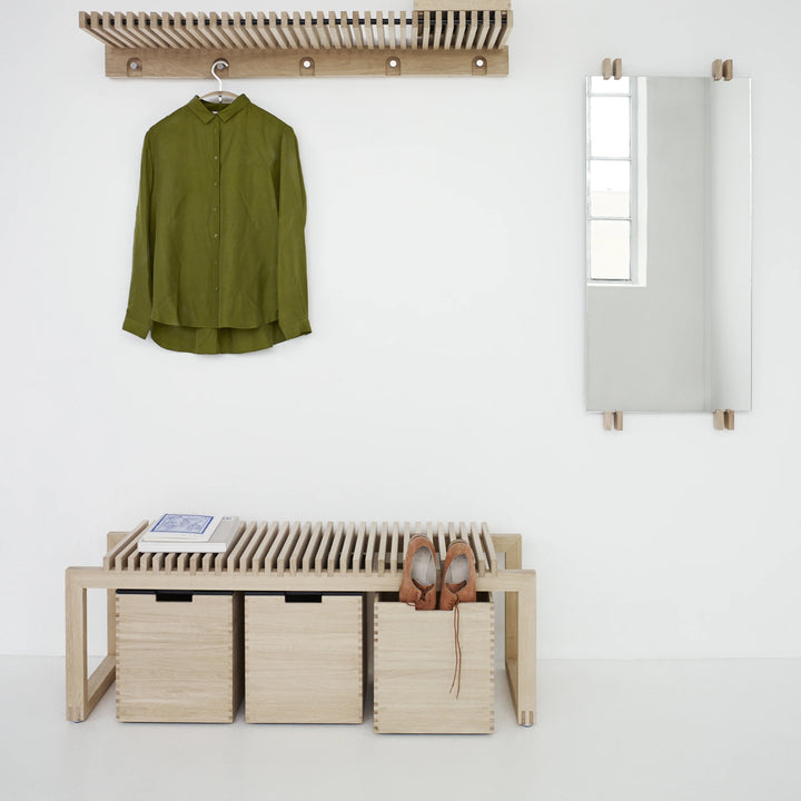 Green shirt hanging on a rack above a wooden bench with storage bins.