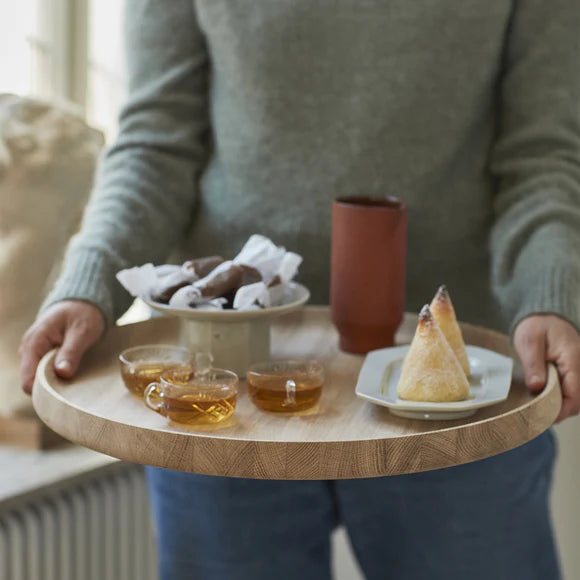 Person holding a wooden tray with tea and snacks indoors
