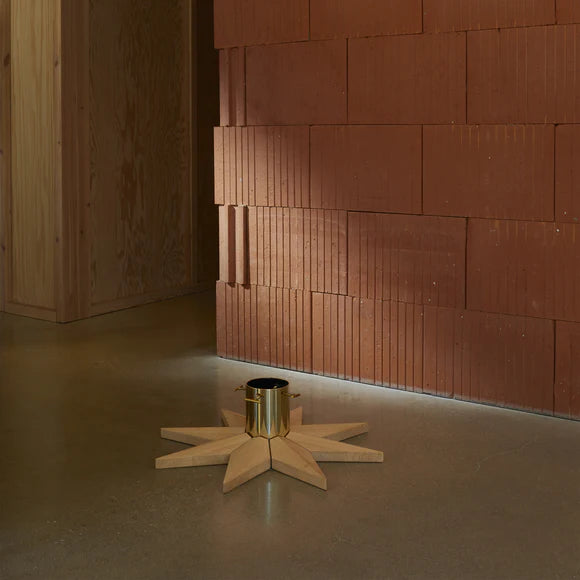 Wooden star-shaped stand with a metallic and oak base against a brick wall.