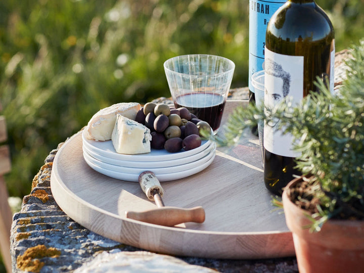 Outdoor setting with a cheeseboard, wine, and olives on a wooden table.