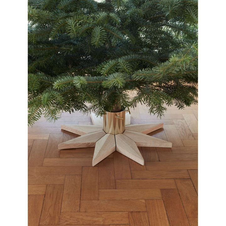Wooden Christmas tree stand with a decorated Christmas tree on a wooden floor.